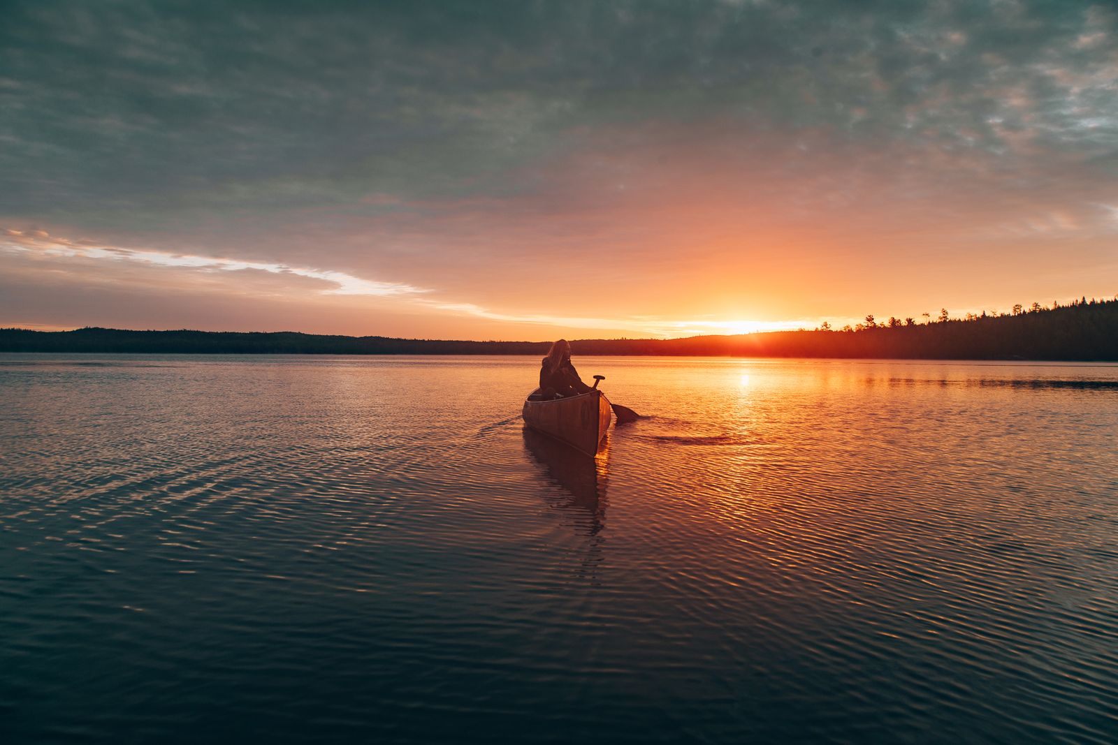A canoeist paddling a lake near Ely at sunset, in the country of the Boundary Waters Canoe Area